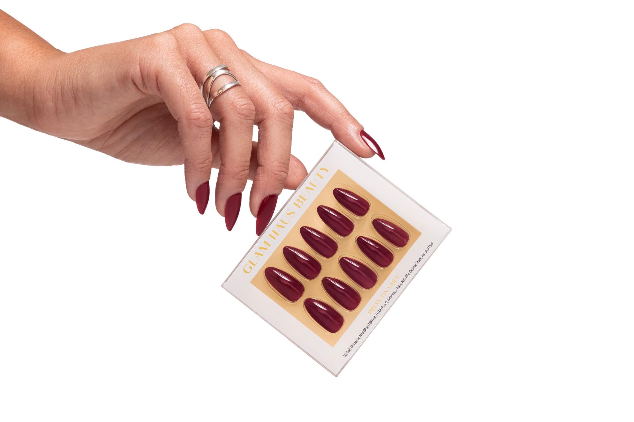 close-up of a hand holding Glam Has Beauty press-on nails box with gold accents. Nails color Burgandy red. Nails shape medium almond