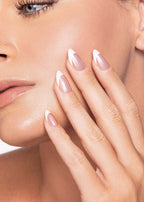 Close-up of a woman's face with a hand gently touching her cheek, showcasing smooth skin and well-manicured chrome French Tip nails. 