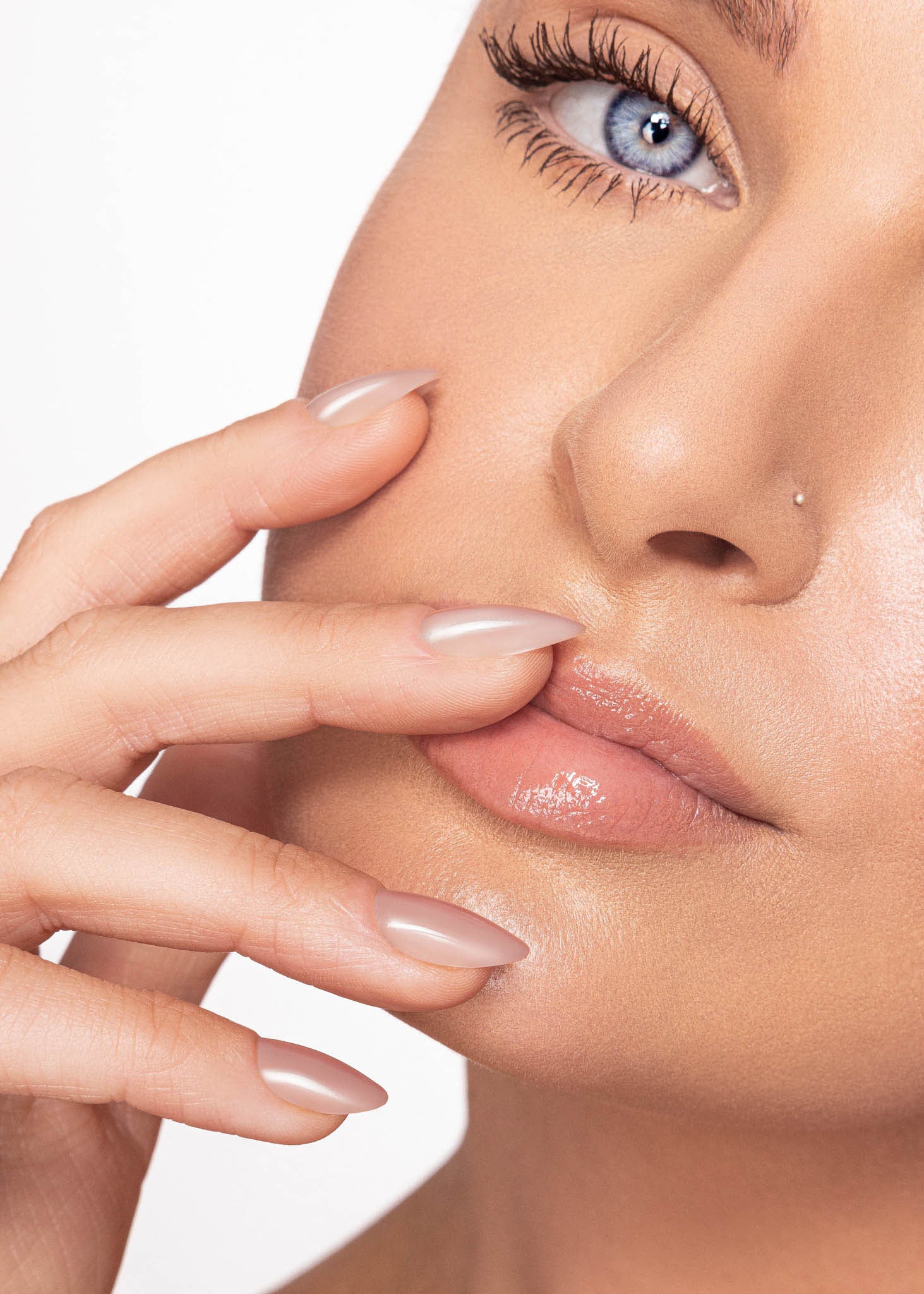 Close-up of a woman's face with a focus on her lips and hand wearing chrome pink almond shaped nails