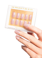 Set of false nails in a Glam Haus Beauty packaging with a hand displaying the nails. Pink color nails, square shape